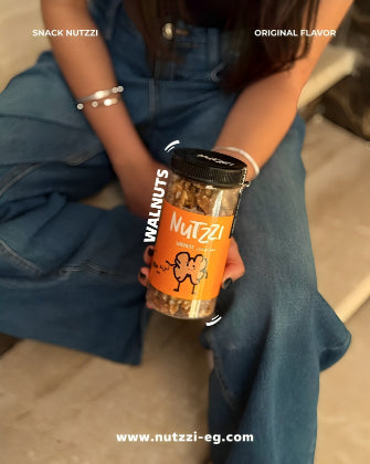 Person holding a jar of Nutzzi walnuts with branding and website information.