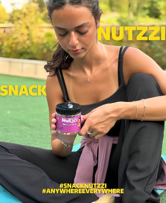 Woman sitting outdoors holding a Nutzzi snack container with greenery in the background